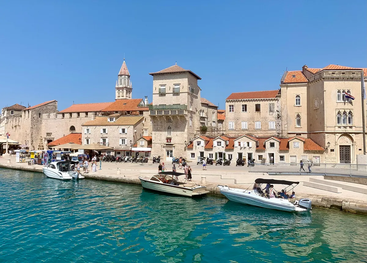 The old town waterfront of Trogir seen from the water, with small motorboats tied along the quay and turquoise water in front.
