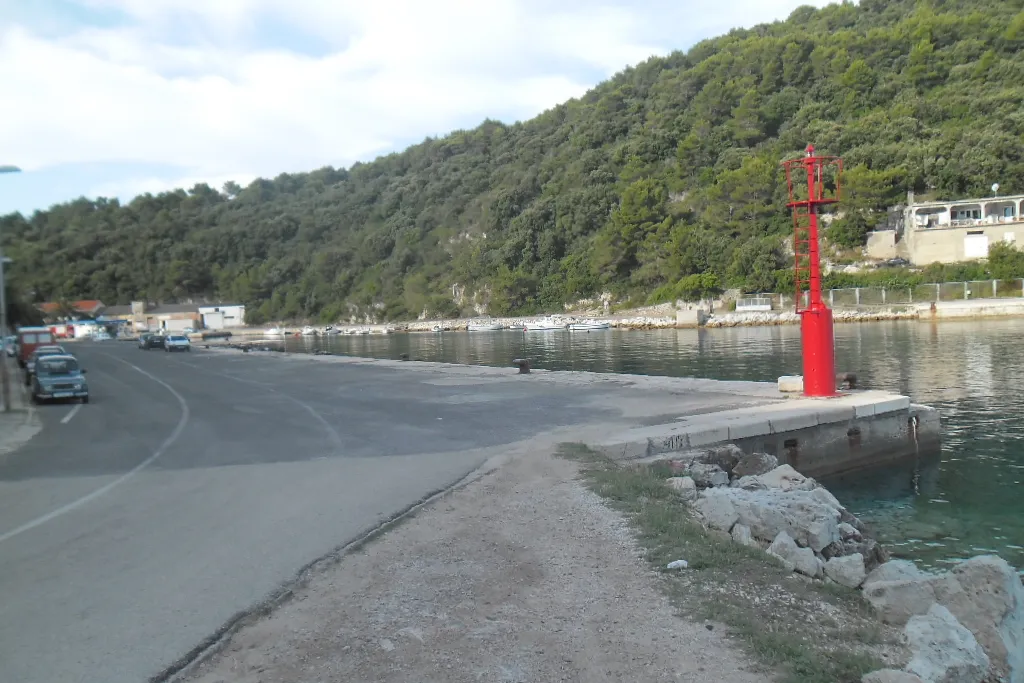 The ferry port of Ubli on Lastovo: the concrete quay with its red harbour light, calm water and wooded hills behind