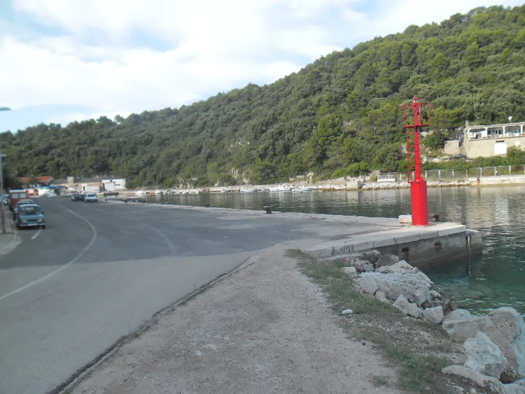 The ferry port of Ubli on Lastovo: the concrete quay with its red harbour light, calm water and wooded hills behind