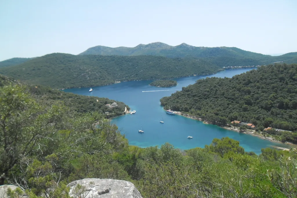 Vejo Lago on Lastovo from Jurjev vrh: a long blue bay between wooded hills, with a small islet, yachts at their moorings and Pasadur on its shore