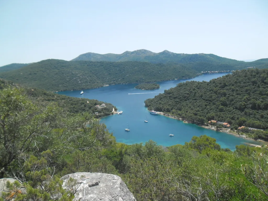 Vejo Lago on Lastovo from Jurjev vrh: a long blue bay between wooded hills, with a small islet, yachts at their moorings and Pasadur on its shore