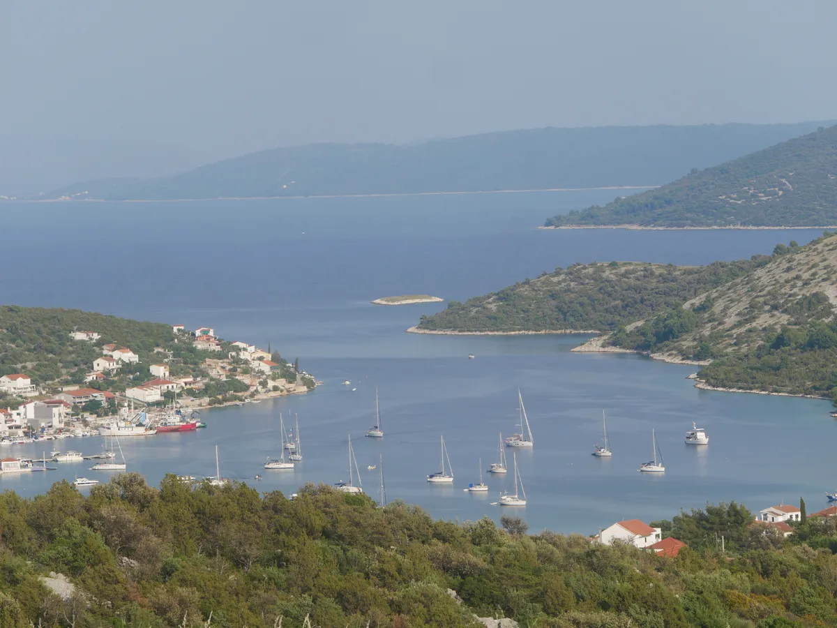 Vinišće bay seen from the hillside, with yachts at anchor, the village waterfront and wooded headlands around the inlet