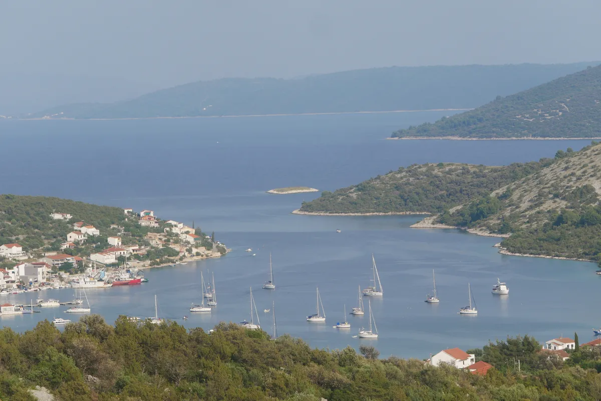 Vinišće bay seen from the hillside, with yachts at anchor, the village waterfront and wooded headlands around the inlet