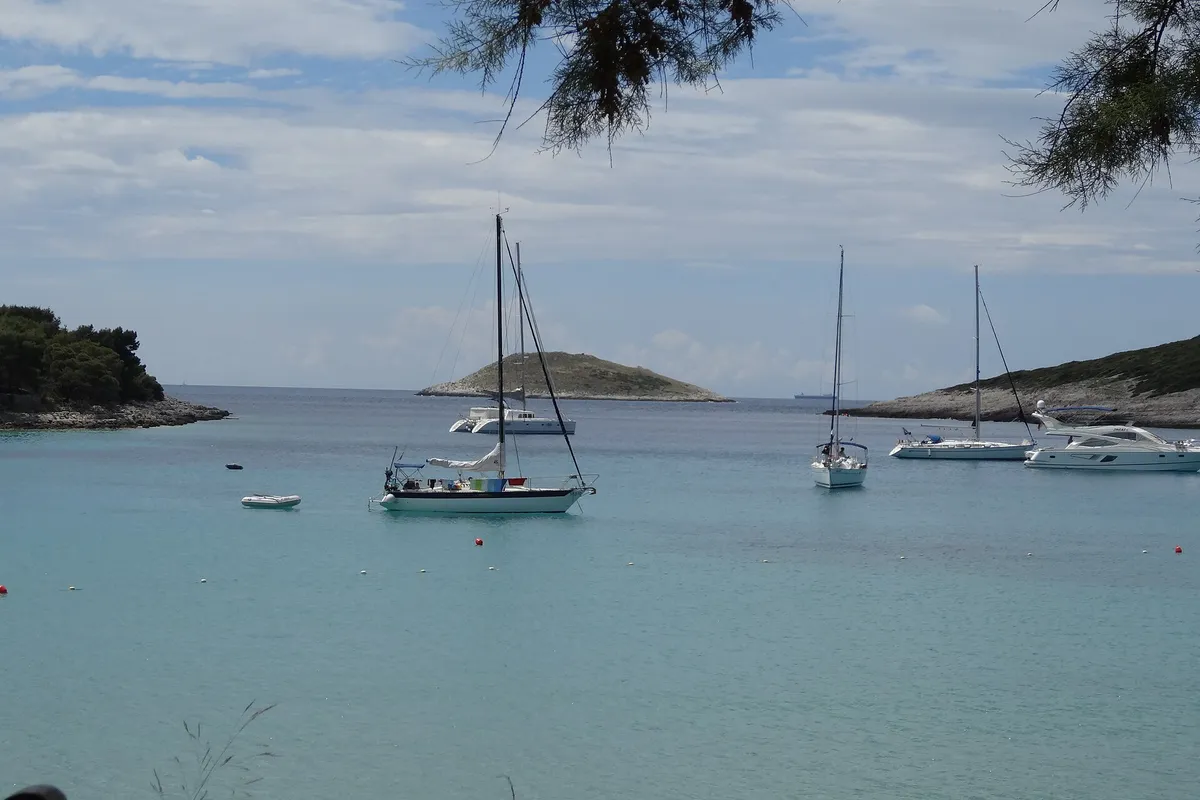 Vinogradišće bay on Sveti Klement from the beach at its head, yachts on the buoys in pale turquoise water and the islet of Stambedar at the mouth