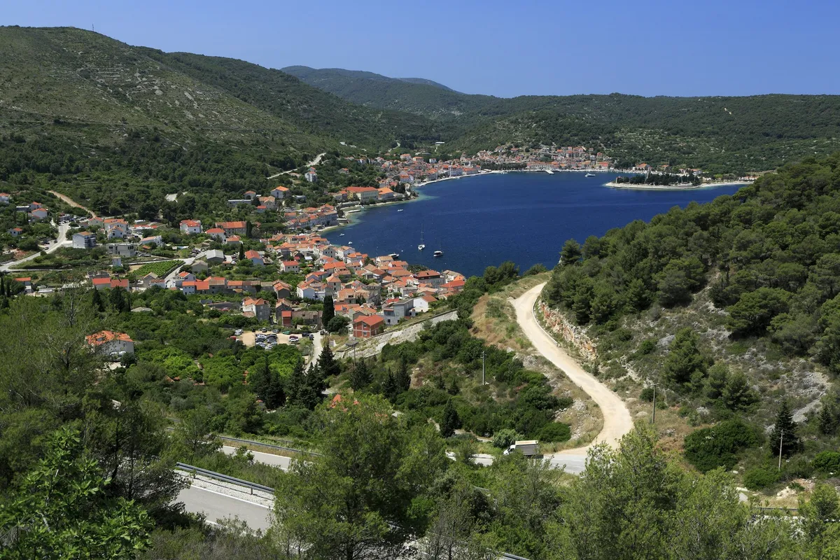 The bay of Vis from the road above Kut: the houses of Kut in front, the long harbour with the town of Vis along its far shore and the Prirovo peninsula, framed by green hills
