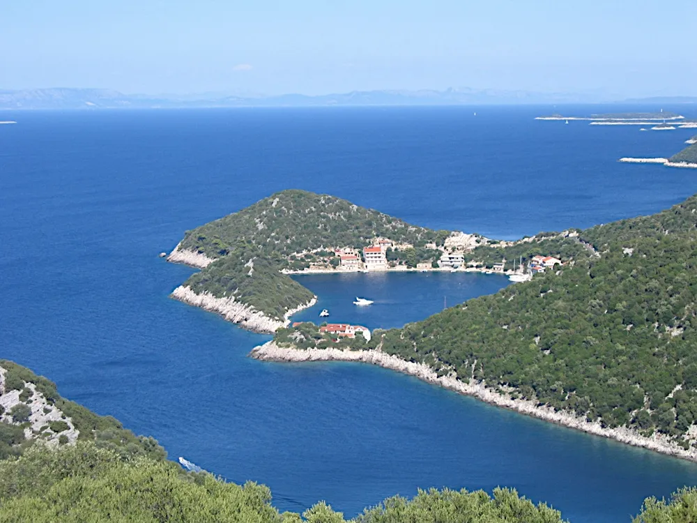 Zaklopatica bay on Lastovo from the hillside above, with the village and its quay on a wooded point and a few boats in the sheltered bay