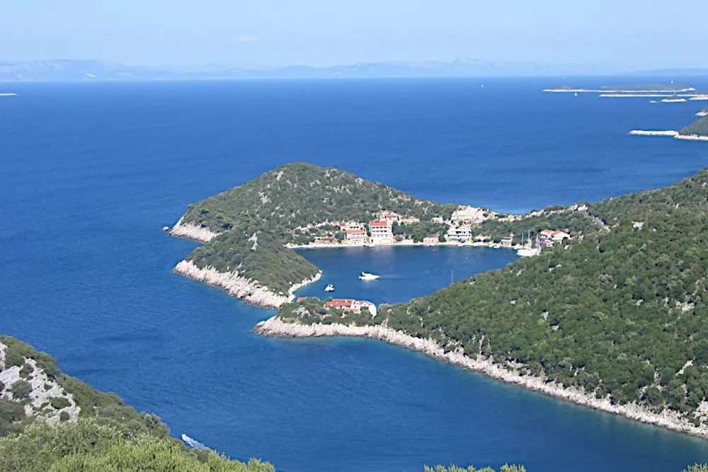 Zaklopatica bay on Lastovo from the hillside above, with the village and its quay on a wooded point and a few boats in the sheltered bay